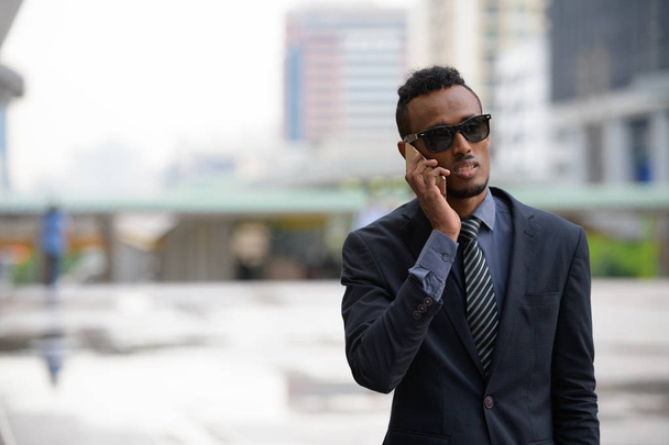 Jeune homme d'affaires africain avec des lunettes de soleil parlant au téléphone à l'extérieur
 - Photo, image