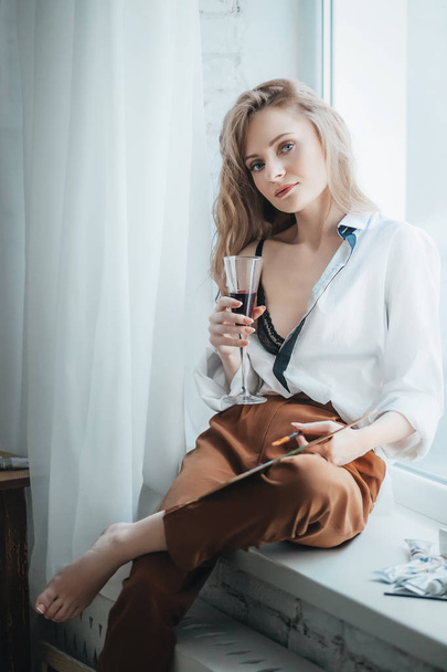 Mooie jonge kunstenaar vrouw poseren in kamer met wijn - Foto, afbeelding