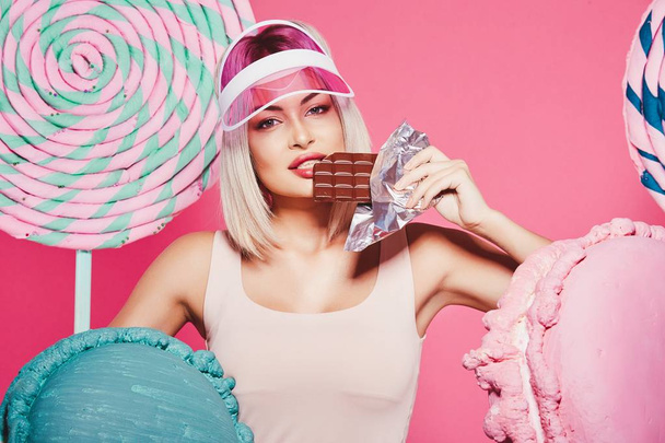 Muchacha atractiva con el pelo rubio de pie con chocolate y dulces enormes sobre fondo rosa
 - Foto, imagen