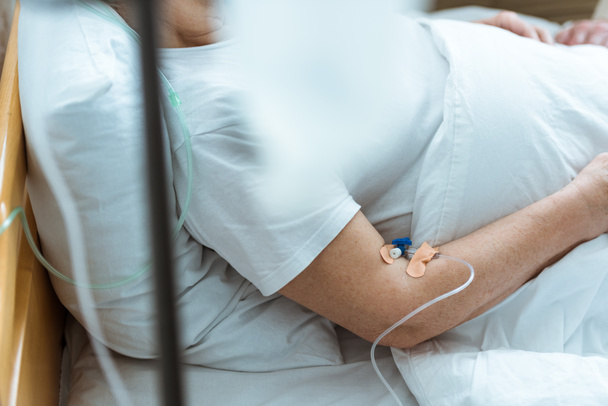 vista parziale della donna malata sdraiata sul letto durante la terapia endovenosa in clinica
 - Foto, immagini