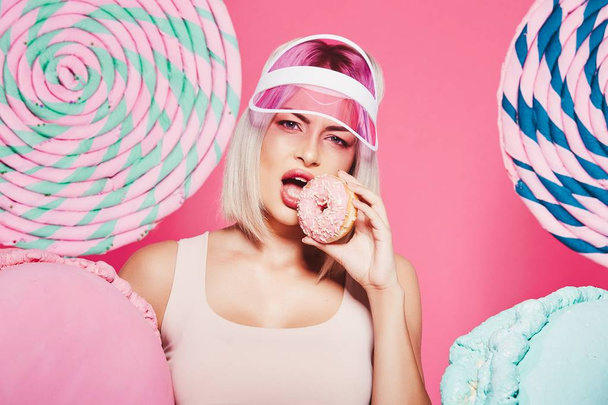 Menina atraente com cabelo loiro de pé com donut e doces enormes no fundo rosa
 - Foto, Imagem