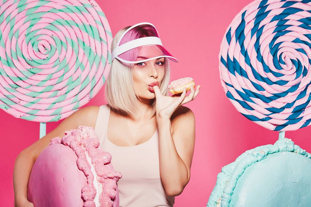 Jolie fille aux cheveux blonds debout avec beignet et d'énormes bonbons sur fond rose
 - Photo, image