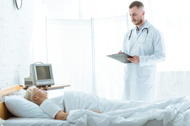 dokter met Klembord en zieke Senior vrouw liggend op bed - Foto, afbeelding