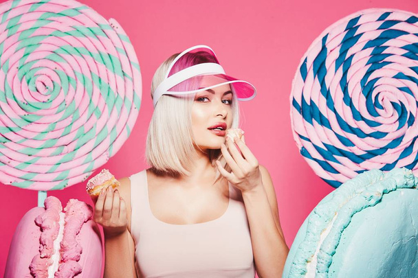 Atraktivní dívka s blond vlasy s koblihy a obrovskými sladkostmi na růžovém pozadí - Fotografie, Obrázek