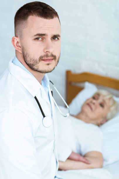 doctor in white coat and sick senior patient lying on bed - Photo, Image
