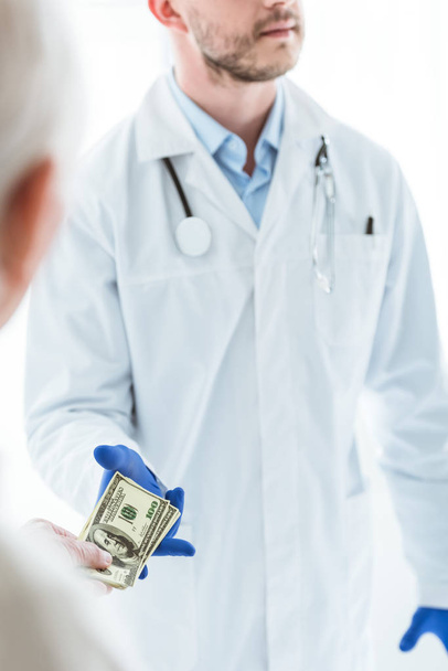 częściowy widok starszy mężczyzna dając łapówku do lekarza na białym - Zdjęcie, obraz