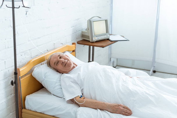 lachende zieke Senior man liggend op bed in kliniek - Foto, afbeelding