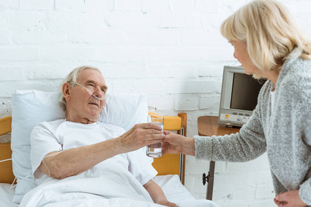 Seniorin schenkt kranken Ehemann im Krankenhaus ein Glas Wasser - Foto, Bild