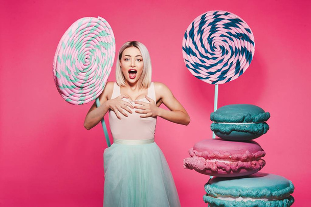 Привлекательная девушка с светлыми волосами, стоящая с огромными сладостями на розовом фоне
 - Фото, изображение