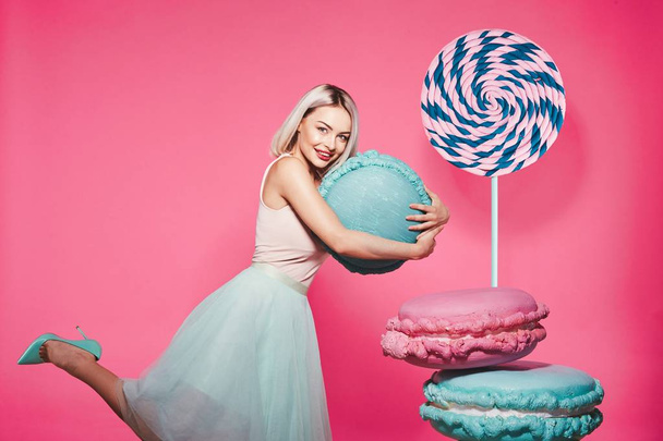 Vonzó lány szőke hajú álló hatalmas édességek rózsaszín háttér - Fotó, kép
