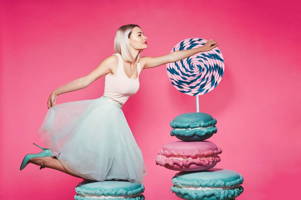 Приваблива дівчина з білявим волоссям, що стоїть з величезними цукерками на рожевому фоні
 - Фото, зображення