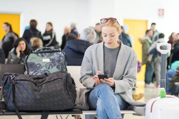 Podróżnik kobiece czytanie na jej telefon komórkowy podczas oczekiwania na pokład samolotu przy bramkach w terminalu lotniska. - Zdjęcie, obraz