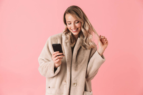 Happy blonde woman wearing in fur coat using smartphone - Foto, afbeelding