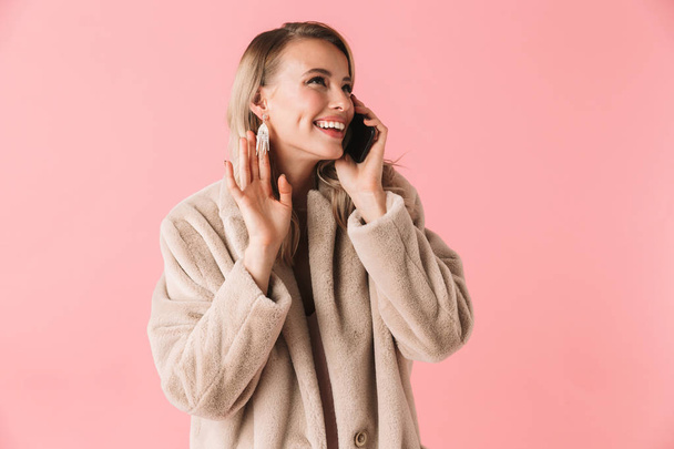 Cheerful blonde woman wearing in fur coat talking by smartphone - Photo, image