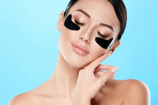 portrait of young woman with nude makeup and eye patches on face on blue background - Photo, Image