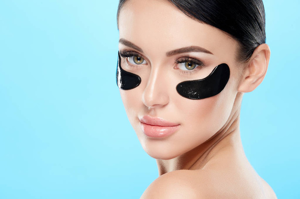 portrait of young woman with nude makeup and eye patches on face on blue background - Photo, Image