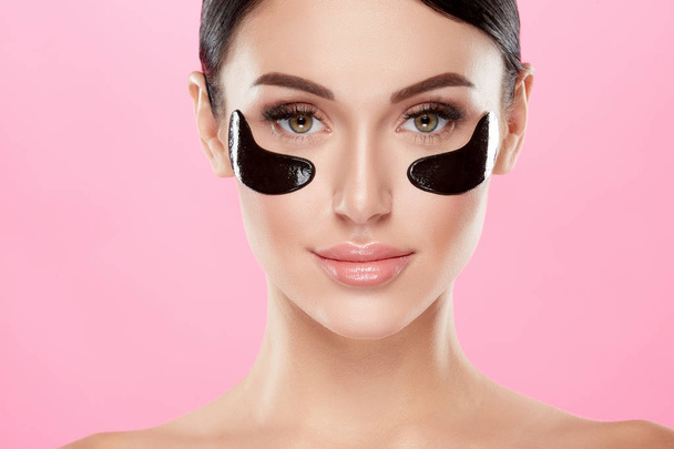 portrait of young woman with nude makeup and eye patches on face on pink background - Photo, Image