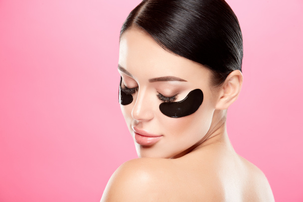 portrait of young woman with nude makeup and eye patches on face on pink background - Photo, Image