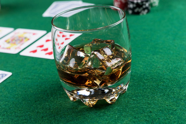 Lasi viskiä jäällä pokeripöydällä korteilla ja sipseillä
 - Valokuva, kuva