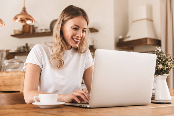 Portrait of young blond woman working on laptop and drinking cof - Photo, Image