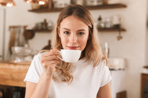 Portrait of young blond woman drinking coffee while sitting in c - Fotoğraf, Görsel