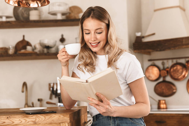 Portrait of caucasian blond woman reading book and drinking tea  - Foto, Imagem