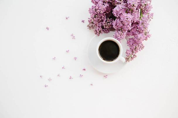 Cup of coffee and lilac branch on white textured background - Фото, изображение