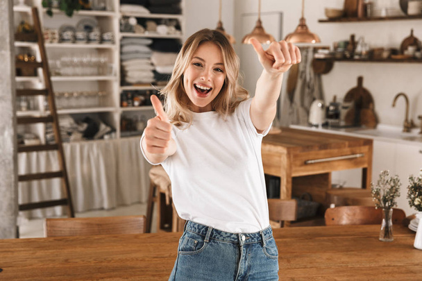 Portrait of happy blond girl smiling and showing thumb up while  - Fotoğraf, Görsel