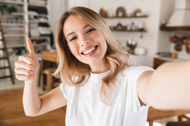 Image closeup of cheery blond woman showing thumb up while takin - Zdjęcie, obraz