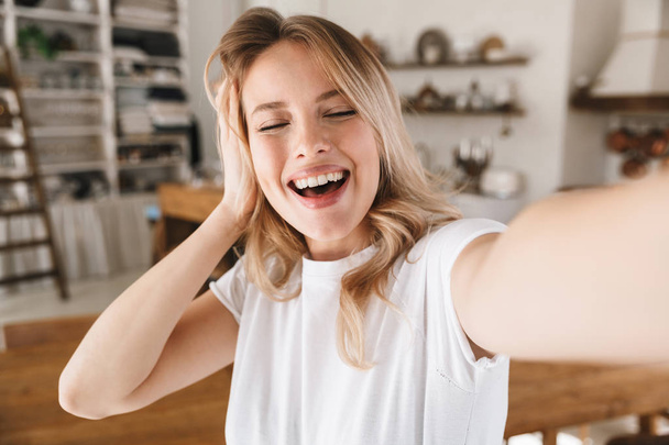 Image closeup of joyful blond woman laughing while taking selfie - 写真・画像