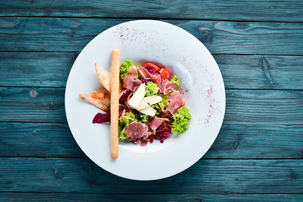 Vegetable salad with brie cheese and prosciutto. In the plate. Top view. Free space for your text. Rustic style. - Photo, Image