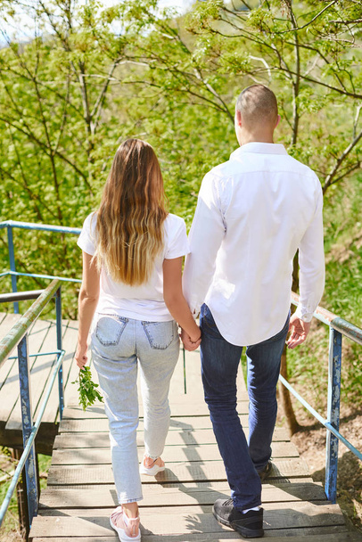 πλάτες των νεαρών αγκάλιασμα ζευγάρι στις σκάλες στο πράσινο πάρκο-δύο ζευγάρια των χεριών στην αγάπη αγκαλιάζονται τρυφερά - Φωτογραφία, εικόνα