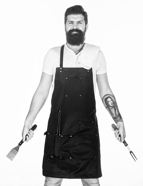 Professional barbecue. Bearded man with barbecue fork and spatula in hands. Grill cook using portable barbecue cooking tools. Hipster holding stainless steel tools for preparing barbecue foods - Φωτογραφία, εικόνα