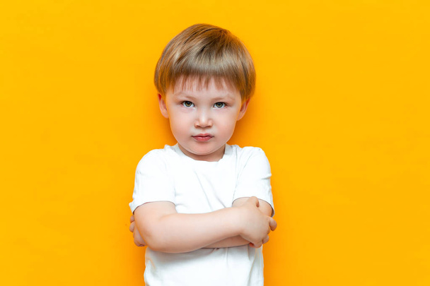 Portrait of angry little boy with arms folded isolated on yellow background. Sad and unhappy child. Upset toddler boy - Zdjęcie, obraz