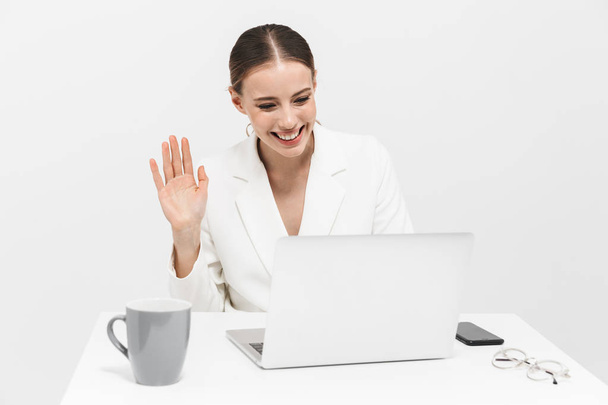 Happy woman posing isolated over white wall background using laptop computer waving. - Valokuva, kuva