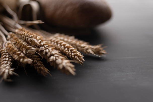 close-up of wheat grains in a spikelet, dark bread lies nearby - Foto, afbeelding