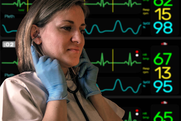 Kobieta lekarz lub pielęgniarka stawia w stetoskop w uszach. Elektrokardiogram Screen monitor cicho niewyraźne na tle. Kobieta nosi mundur i niebieskie rękawice lateksowe. Nie patrząc na kamerę - Zdjęcie, obraz