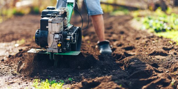 közelről fotó fiatal gazda Kertész művelni talaj talajban ROTOTILLER, kormányrúd traktor, cutivator, miiling gép, előkészíti a növény termés, tavasz. modern gazdálkodás, technológiai mezőgazdaság - Fotó, kép