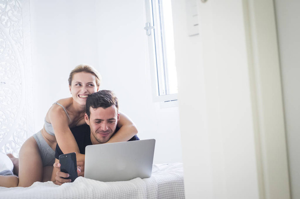 Ευτυχισμένο νεαρό όμορφο ζευγάρι σε παιχνιδιάρικη δραστηριότητα στο σπίτι στο υπνοδωμάτιο στο λευκό κρεβάτι  - Φωτογραφία, εικόνα