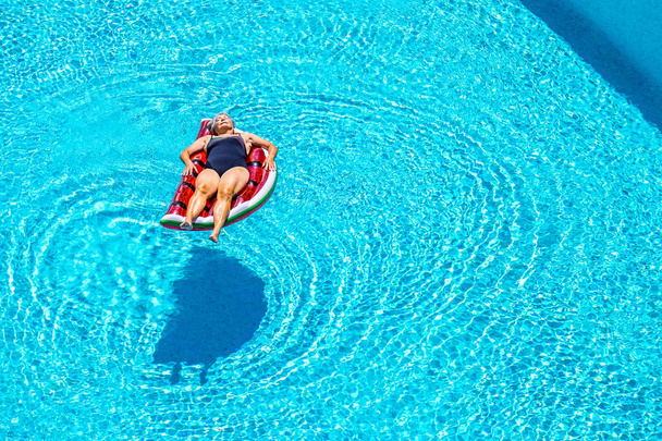 Vanhempi nainen rentouttava punainen vesimeloni patja uima-altaassa
  - Valokuva, kuva