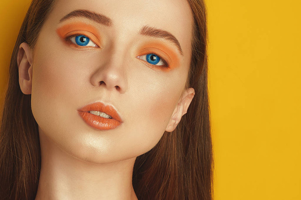 Multi-colored lenses for eyes. Blue lenses, green lenses. Beauty Model Girl with orange professional makeup. Orange eye shadow and lipstick.Orange background. - Photo, Image