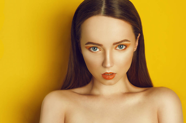 Beauty Model Girl with yellow / orange professional makeup. Orange eye shadow and lipstick  Fashion woman with long, straight hair. High fashion trend make up. Yellow / orange background. Portrait. - 写真・画像
