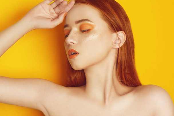 Beauty Model Girl with yellow / orange professional makeup. Orange eye shadow and lipstick  Fashion woman with long, straight hair. High fashion trend make up. Yellow / orange background. Portrait. - Photo, Image