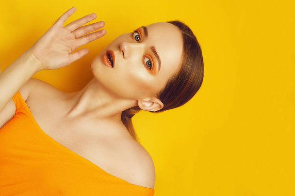 Beauty Model Girl with yellow / orange professional makeup. Orange eye shadow and lipstick  Fashion woman with long, straight hair. High fashion trend make up. Yellow / orange background. Fashion - Photo, Image