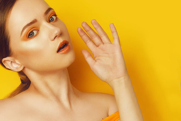 Beauty Model Girl with yellow / orange professional makeup. Orange eye shadow and lipstick  Fashion woman with long, straight hair. High fashion trend make up. Yellow / orange background. Fashion - 写真・画像