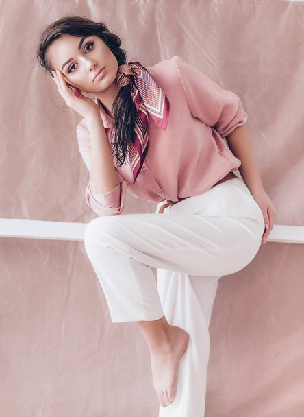 Красивая молодая женщина позирует в розовой блузке и белых брюках
 - Фото, изображение