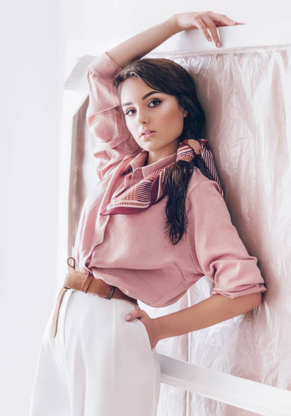 Beautiful young woman posing in pink blouse and white pants - Photo, Image
