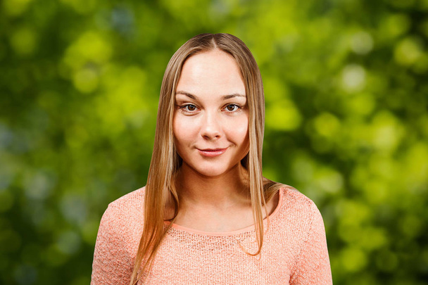 緑のボケの背景にベージュのシャツで美しい笑顔の若い女性のクローズアップ - 写真・画像
