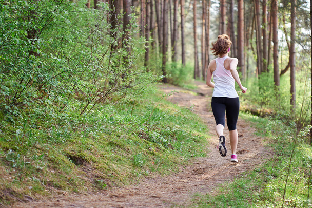 Athletic young woman in pink sneakers run in spring forest - Photo, Image