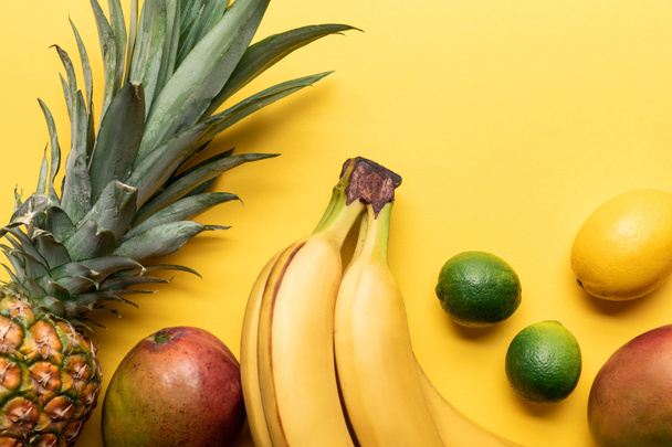 top view of whole ripe bananas, pineapple, citrus fruits and mango on yellow background with copy space - Photo, Image
